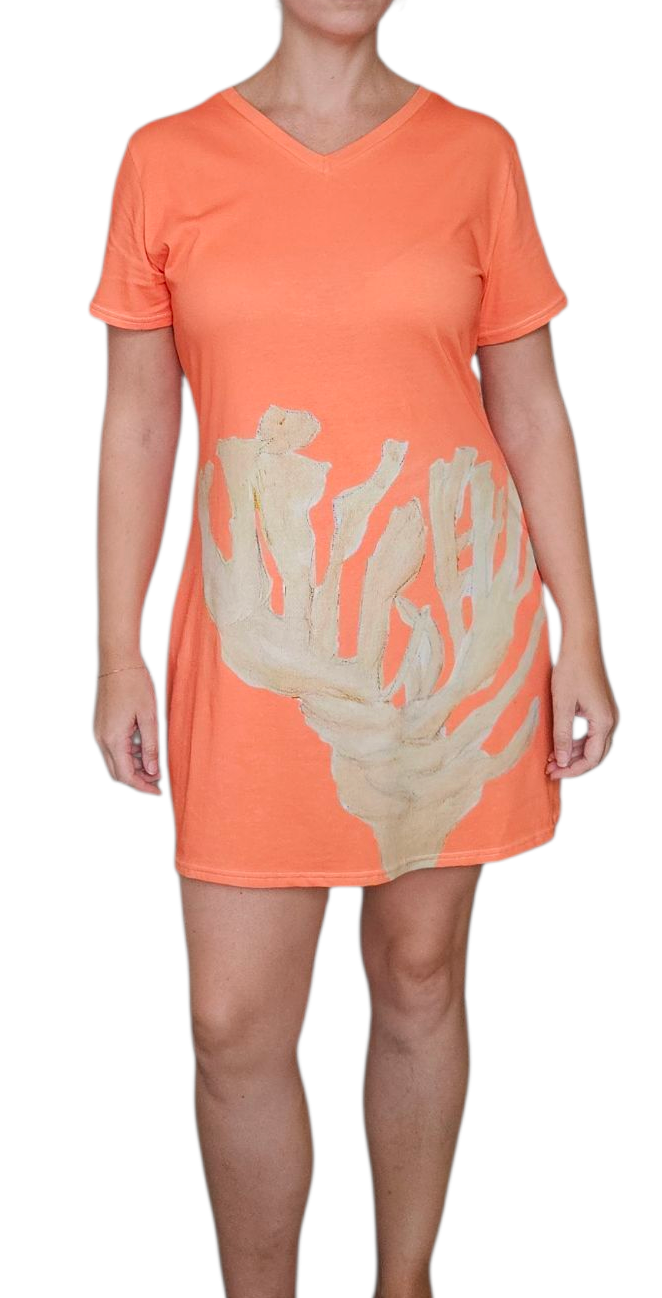 A woman wearing a coral tee shirt dress. The dress is v neck, knee length, and a loose fit. 100% cotton with a hand painted coral on the front across the bottom. A beach vacation dress