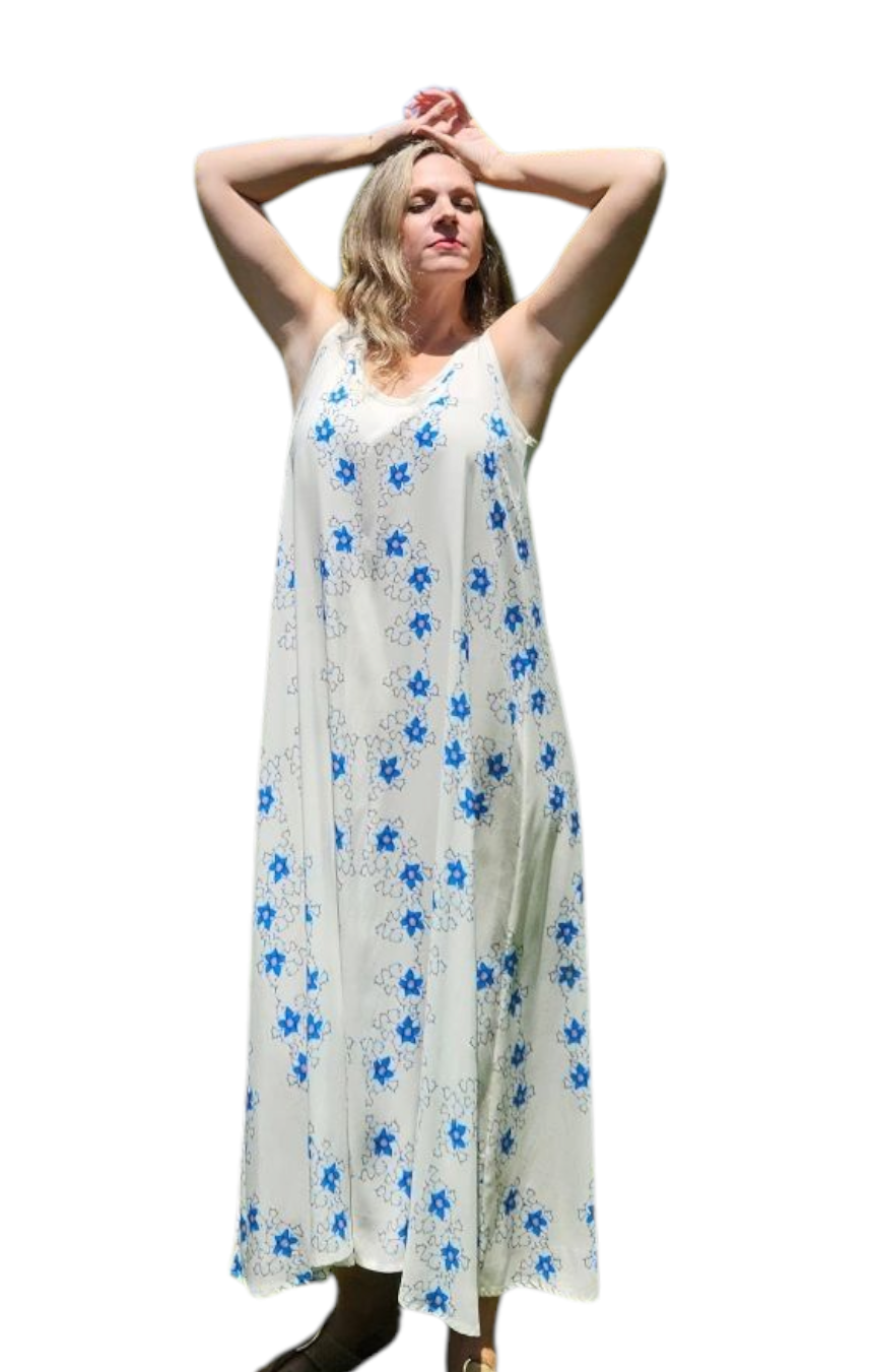 A woman wearing a loose-fitting maxi dress for a beach vacation or a beach day. The vacation dress has small blue flowers in a design. The woman has her arms up by her head.